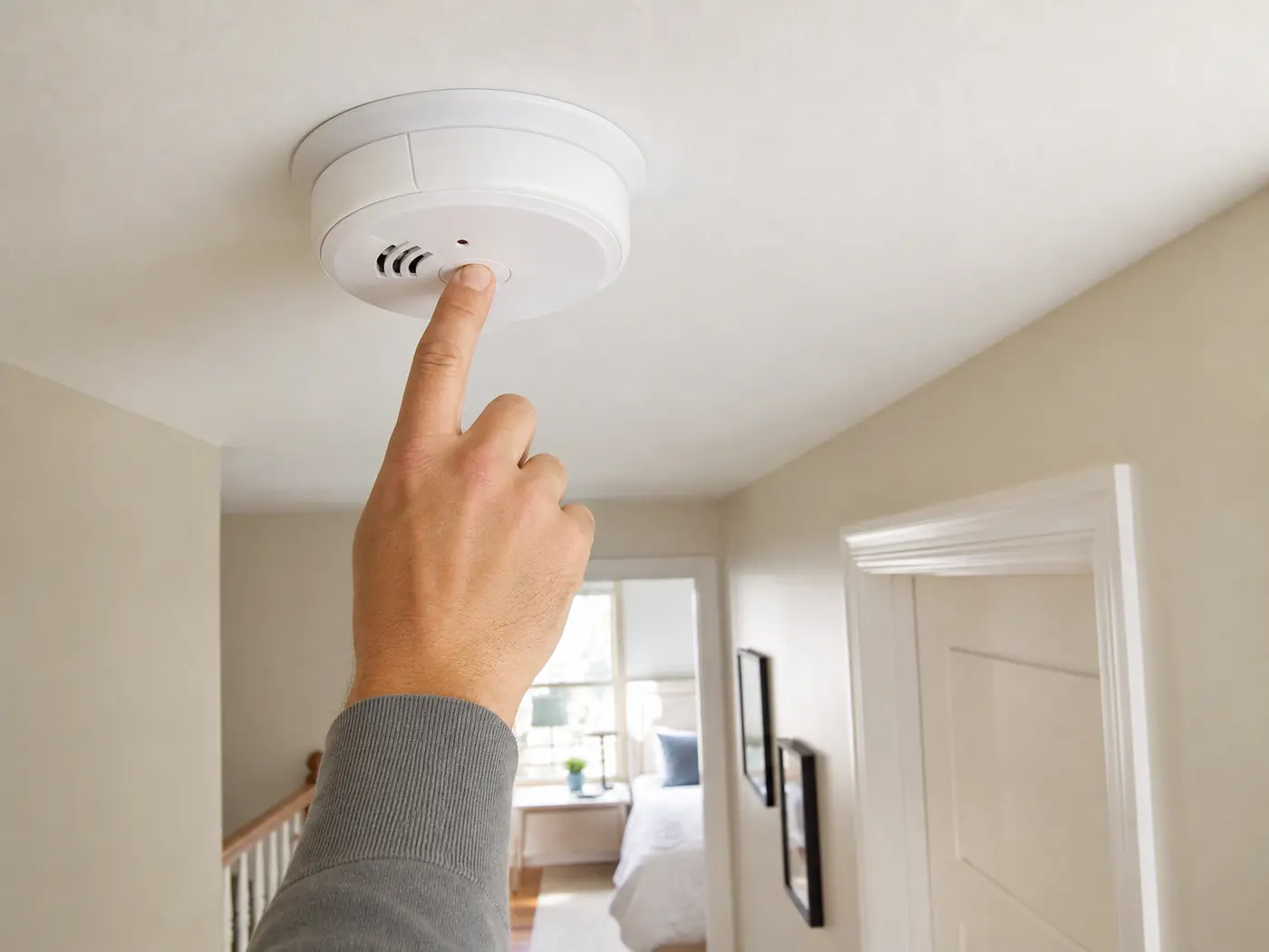 Main appuyant sur le bouton test d’un détecteur de fumée fixé au plafond